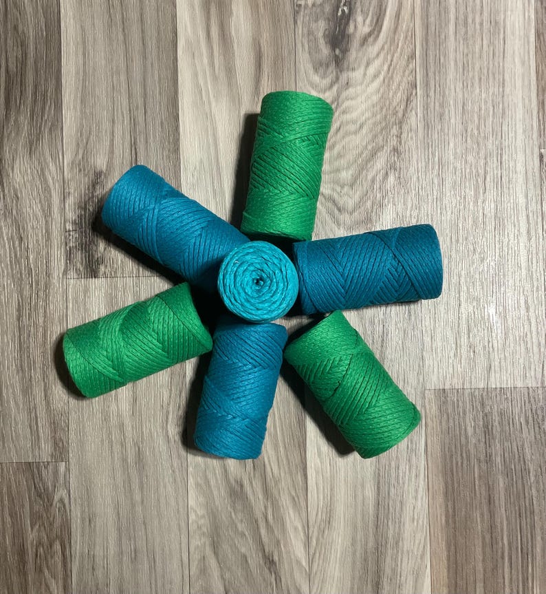 May include: Six spools of twine in teal and green colors arranged in a star shape on a wood floor.