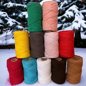 May include: A collection of 10 spools of cotton rope in various colors, including red, green, brown, yellow, pink, white, blue, and tan. The spools are arranged in a pyramid shape on a snowy surface.