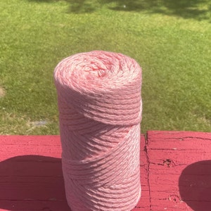 May include: A pink ball of yarn on a red wooden surface. The yarn is made of cotton and is soft to the touch.