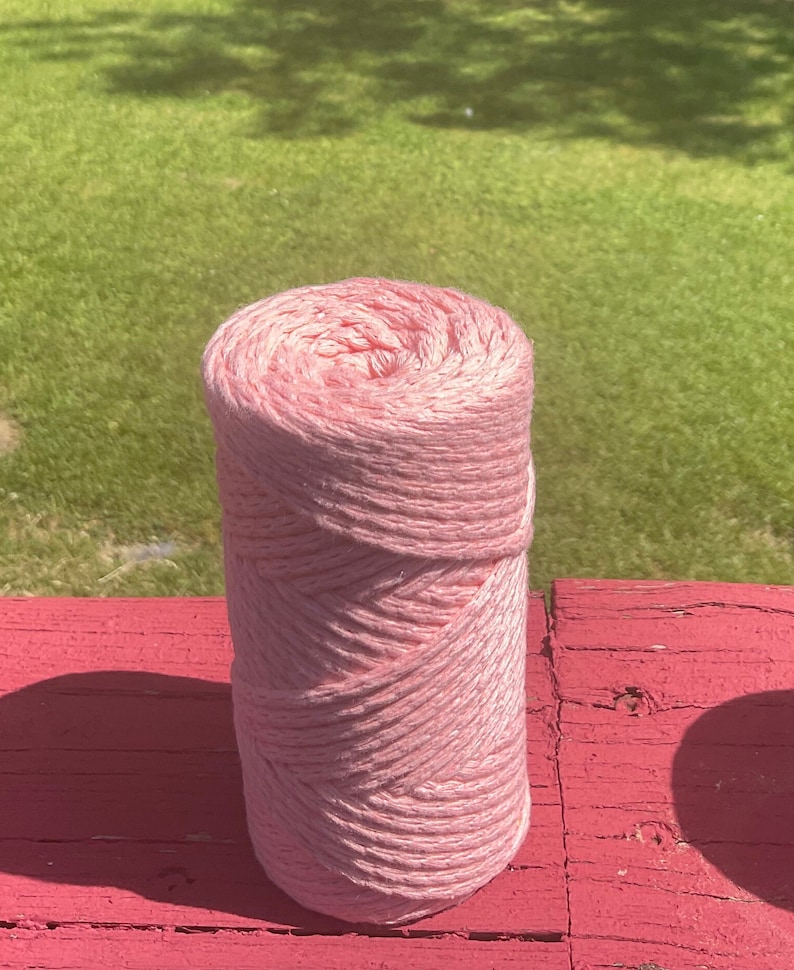 May include: A pink ball of yarn on a red wooden surface. The yarn is made of cotton and is soft to the touch.
