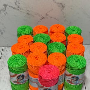 May include: A collection of neon green, orange, and pink spools of string. The spools are arranged in a pyramid shape and have labels that say "Soft n' Strong" and "String Yarn".