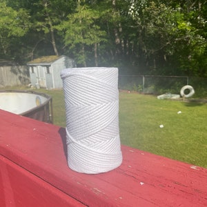 May include: A white roll of thick cotton rope on a red wooden surface. The rope is tightly wound and has a textured surface.