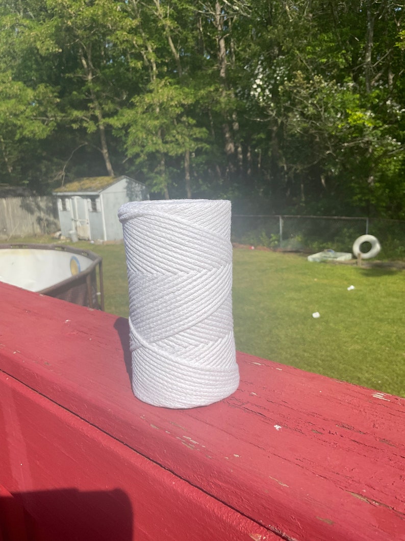 May include: A white roll of thick cotton rope on a red wooden surface. The rope is tightly wound and has a textured surface.