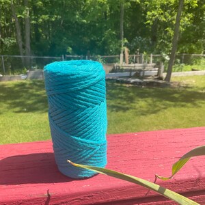 May include: A roll of teal blue cotton rope, sitting on a red wooden surface.
