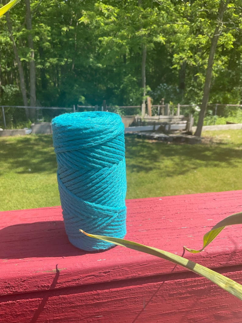May include: A roll of teal blue cotton rope, sitting on a red wooden surface.