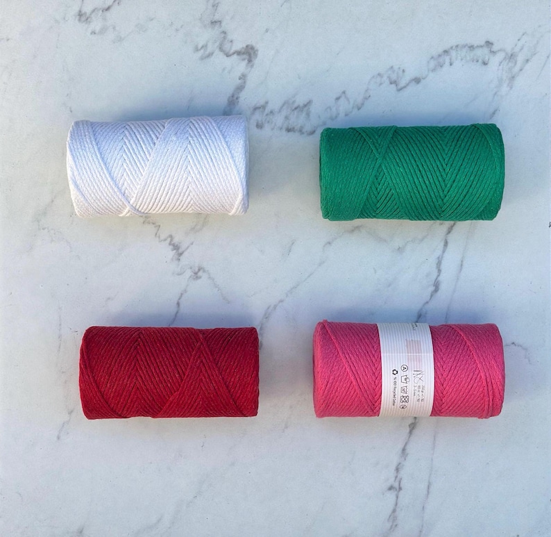 May include: Four spools of cotton cord in different colors: white, green, red, and pink. The spools are arranged in a square pattern on a white marble surface.