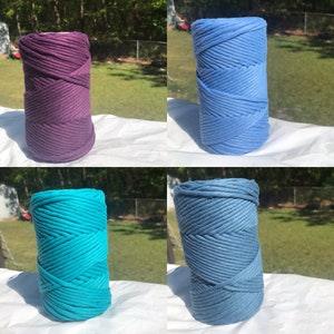 Pode incluir: Quatro rolos de corda de algod&atilde;o em diferentes cores: roxo, azul claro, turquesa e azul escuro. Os rolos est&atilde;o dispostos em uma grade sobre uma superf&iacute;cie branca.