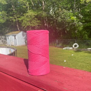 May include: A pink spool of twine, sitting on a red wooden surface. The spool is made of natural fibers and has a rough texture.