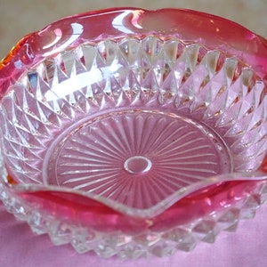 May include: A clear glass bowl with a diamond pattern and a pink rim. The bowl is on a pink surface.