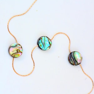 Op de afbeelding: Een gouden ketting met drie iriserende parels van abalone. De parels zijn rond en hebben een natuurlijk, organisch patroon.
