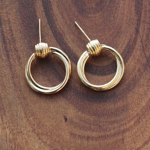 Puede incluir: Un par de pendientes de aro dorados con un detalle de nudo retorcido. Los pendientes son simples y elegantes.