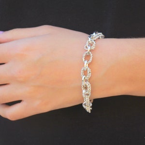May include: A silver chain bracelet with a rope-like design. The bracelet is on a person's wrist.