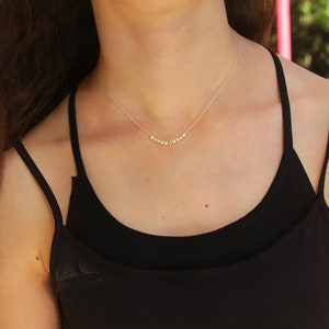 Op de afbeelding: Een zilveren ketting met een rij kleine, ronde kralen. De ketting wordt gedragen door een persoon met lang bruin haar en een zwart tanktop.