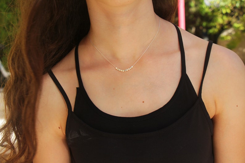 Op de afbeelding: Een zilveren ketting met een rij kleine, ronde kralen. De ketting wordt gedragen door een persoon met lang bruin haar en een zwart tanktop.