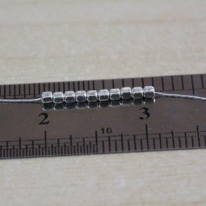 Op de afbeelding: Een close-up van een zilveren metalen kralenketting, gemeten op een liniaal, die laat zien dat de ketting 2,5 cm lang is.