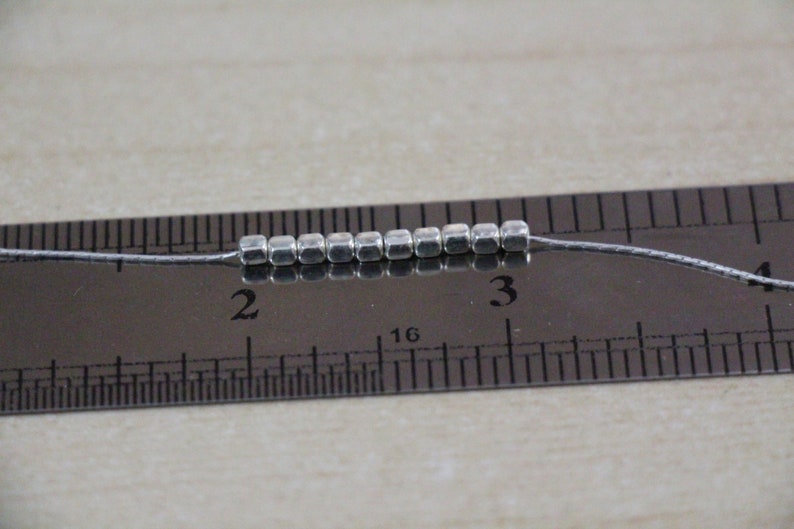 Op de afbeelding: Een close-up van een zilveren metalen kralenketting, gemeten op een liniaal, die laat zien dat de ketting 2,5 cm lang is.