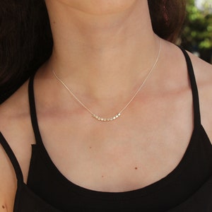 Op de afbeelding: Een zilveren ketting met een delicate ketting en een rij kleine, vierkante kralen.