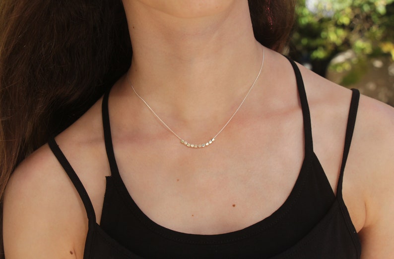 Op de afbeelding: Een zilveren ketting met een delicate ketting en een rij kleine, vierkante kralen.