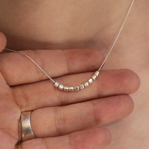 Op de afbeelding: Een zilveren ketting met een delicate ketting en een rij kleine, vierkante kralen.