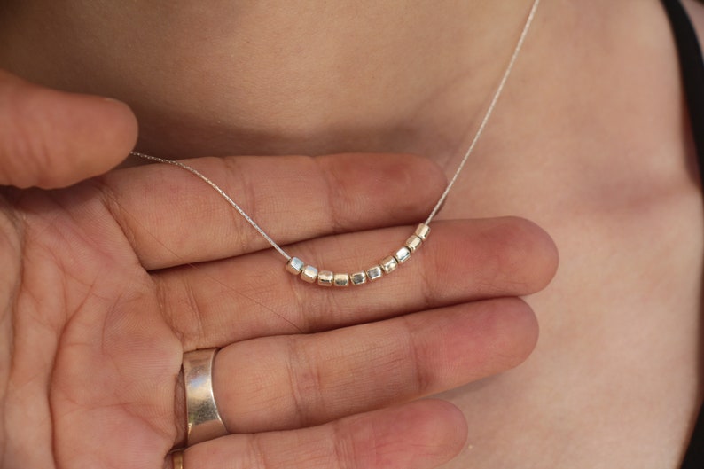 Op de afbeelding: Een zilveren ketting met een delicate ketting en een rij kleine, vierkante kralen.
