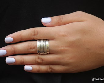 May include: A silver ring with multiple bands stacked on top of each other. The ring is worn on a person's finger.