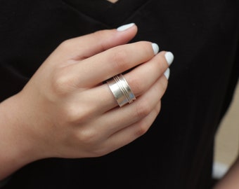 May include: A silver spinning ring with a wide band and a textured surface.