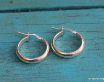 May include: A pair of silver hoop earrings. The earrings are smooth and have a rounded shape.