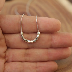 Op de afbeelding: Een zilveren ketting met een ketting en een rij kleine, vierkante kralen.