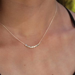 Op de afbeelding: Een zilveren ketting met een rij kleine, vierkante kralen.