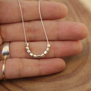 Op de afbeelding: Een zilveren ketting met een ketting en een rij kleine, vierkante kralen.