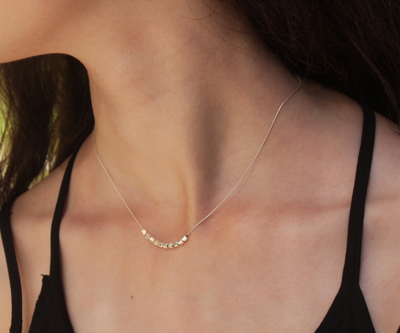 Op de afbeelding: Een zilveren ketting met een delicate ketting en een rij kleine, vierkante kralen.