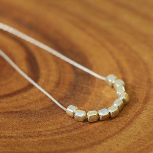 Op de afbeelding: Een zilveren ketting met een rij kleine, vierkante kralen.