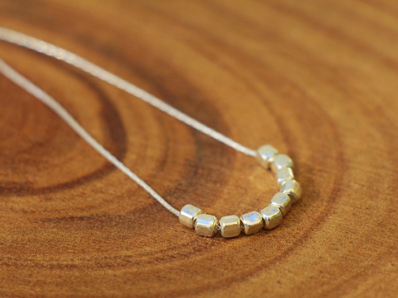 Op de afbeelding: Een zilveren ketting met een rij kleine, vierkante kralen.