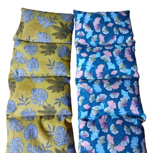 Può includere: Due cuscini lunghi rettangolari in tessuto con chiusura a zip. Il cuscino a sinistra è giallo con un motivo a foglie grigie. Il cuscino a destra è blu con un motivo a foglie rosa e bianche.