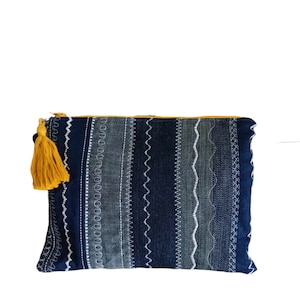 Peut inclure: Une pochette zippée à rayures bleues et blanches avec un pompon jaune. La pochette est en jean et présente différents motifs de couture.