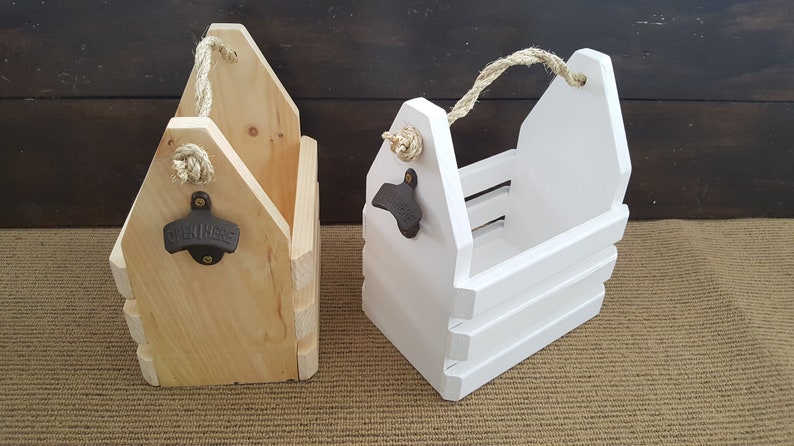 May include: Two wooden bottle carriers with rope handles and bottle openers. One carrier is natural wood and the other is painted white.