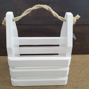 May include: White wooden crate with a rope handle. The crate has a rustic look and is perfect for storage or display.
