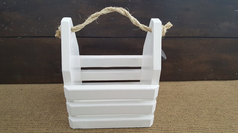 May include: White wooden crate with a rope handle. The crate has a rustic look and is perfect for storage or display.
