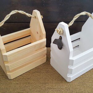 May include: Two wooden bottle carriers with rope handles. One is natural wood and the other is painted white. Both have bottle openers attached.