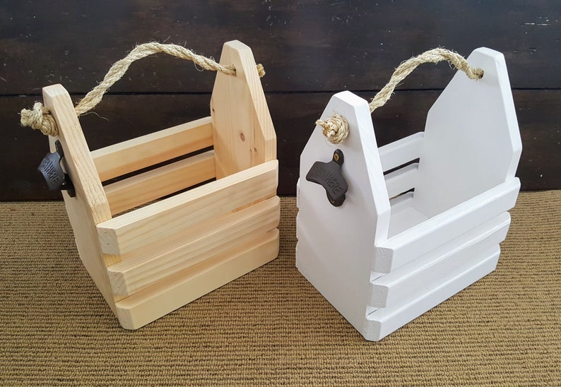 May include: Two wooden bottle carriers with rope handles. One is natural wood and the other is painted white. Both have bottle openers attached.