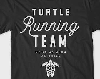 May include: Black t-shirt with white text that reads "TURTLE RUNNING TEAM WE'RE AS SLOW AS HELL" and a graphic of a sea turtle.