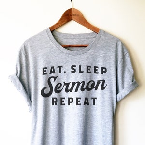 May include: A heather grey t-shirt with black text that reads "Eat, Sleep, Sermon, Repeat".