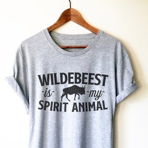 Può includere: Una maglietta grigia con una grafica nera che dice "Wildebeest -is- my- SPIRIT ANIMAL" con una silhouette di uno gnu.