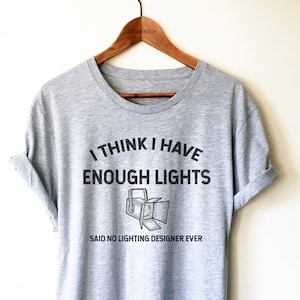 May include: Gray t-shirt with the text "I think I have enough lights said no lighting designer ever" and a drawing of a spotlight.