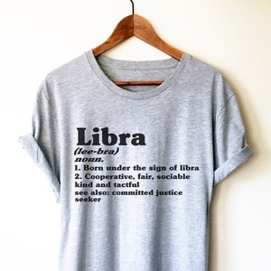 May include: Gray t-shirt with a black graphic that defines the word "Libra" as a noun. The definition includes the phrase "Born under the sign of libra" and "Cooperative, fair, sociable, kind and tactful".