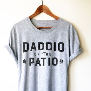 May include: Gray t-shirt with black text that reads "Daddio of the Patio" with a flame graphic on either side of the word "Patio".