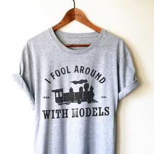 May include: A gray t-shirt with a black print of a train and the text "I fool around with models -S.S.P.- -CO.-".