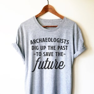 Peut inclure: T-shirt gris avec un texte noir qui dit "Les archéologues déterrent le passé -pour sauver l'avenir-".