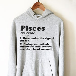 May include: Gray hooded sweatshirt with the word "Pisces" in black bold letters and a definition of the word. The definition includes the phrase "Born under the sign of pisces." and "Caring, empathetic instinctive and creative."