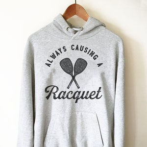 May include: Gray hooded sweatshirt with the text "ALWAYS CAUSING A Racquet" and a graphic of two crossed tennis rackets.